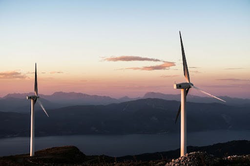 Two Wind Turbines Against A Mountain Range Backdrop at Dusk