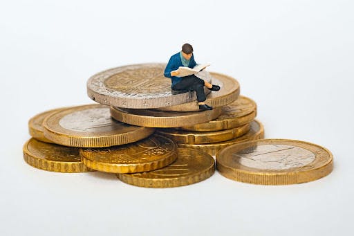 Miniature man figurine sitting on coins